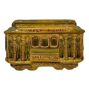Peut inclure: Un tramway de San Francisco en céramique jaune avec les mots "Powell & Hyde" et "San Francisco" sur le côté. Le tramway a trois fenêtres et est décoré de figurines de personnes.