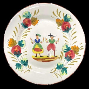Könnte beinhalten: Weiße Keramikplatte mit handgemaltem Design. Die Platte zeigt ein zentrales Bild von zwei stilisierten Figuren in traditioneller Kleidung, umgeben von floralen und Blattmotiven in Rot, Grün, Gelb und Gold. Der Rand ist braun.