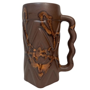 May include: A brown ceramic mug with a wavy handle and a diamond pattern. The mug has a brown glaze with a copper-colored design.