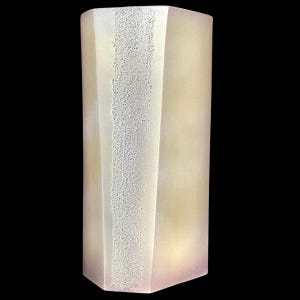 Puede incluir: Un objeto decorativo alto y rectangular, de color blanquecino, con una franja vertical texturizada en el centro. El objeto tiene un diseño facetado y una suave combinación de colores degradados, que transita de un amarillo pálido a un tono rosa claro. El fondo es negro.