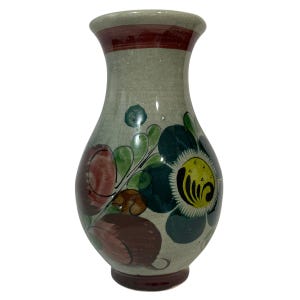 May include: A ceramic vase with a light grey background and a floral design in shades of green, red, yellow, and black. The vase has a rounded body and a narrow neck.