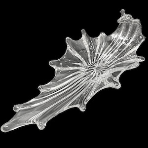 Puede incluir: Cuenco decorativo de vidrio transparente con una forma asimétrica única. El cuenco tiene una depresión circular central con líneas radiales y una serie de bordes ondulados y puntiagudos. El vidrio es transparente.