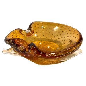 May include: A vintage amber glass ashtray with a textured bubble design. The ashtray has a unique, wavy shape and a clear glass base.