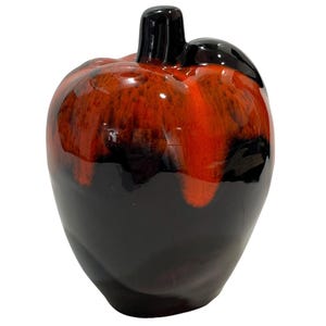 May include: A ceramic apple-shaped decorative object featuring a glossy finish with a colour gradient that transitions from a deep, dark black at the base to a vibrant, bright orange at the top, complete with a small black stem and leaf detail.