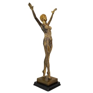May include: A gold-toned sculpture of a woman standing on a black base. The woman is depicted with her arms raised above her head, and her body is covered in a textured pattern.