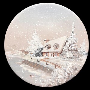 May include: A circular painting depicting a winter landscape with a small house featuring a snow-covered roof, surrounded by frost-laden trees and a frozen shoreline. The scene is rendered in shades of white, beige, and brown with visible snowfall.
