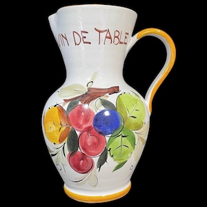 May include: White ceramic jug with a yellow handle and a painted design of red, yellow, green and blue fruit. The jug has the words "Vin de Table" written on the front.