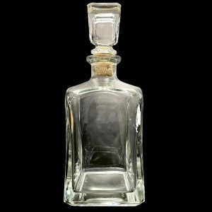 Op de afbeelding: Een glazen karaf met een vierkante body en een vierkante stop. De karaf heeft een kurken stop.