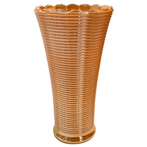 Pode incluir: Um vaso de vidro alto e canelado com uma borda festonada. O vaso é de cor pêssego claro com um acabamento brilhante.