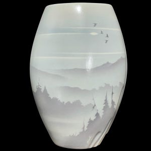 Op de afbeelding: Een witte keramische vaas met een landschapsontwerp. De vaas heeft een bergketen, bomen en vliegende vogels in grijstinten en blauw. De vaas heeft een gladde, glanzende afwerking en een gebogen vorm.