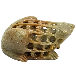 Op de afbeelding: Een gebeeldhouwde kikker sculptuur in tinten bruin en groen. De kikker zit met ingewikkelde opengewerkte details over het hele lichaam. De sculptuur heeft een gladde, gepolijste afwerking.