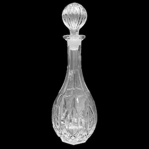 Op de afbeelding: Een glazen karaf met een transparante, getextureerde oppervlakte en een ronde stop. De karaf heeft een brede basis en een smalle hals.