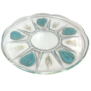 May include: Clear glass serving platter with a scalloped edge. The platter features a central oval section and several pie-shaped compartments. Each compartment is decorated with teal leaf designs and gold accents.
