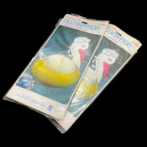 May include: Two packages of nesting stork decorations. Each package features a stork illustration with a white body, pink beak, and a yellow honeycomb skirt. The packages are labeled "DECORATION" and "Cigogne couveuse".