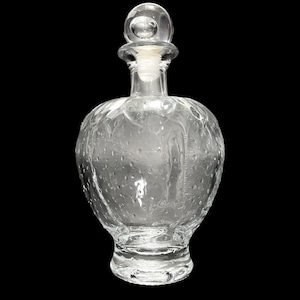 Op de afbeelding: Een heldere glazen fles met een getextureerd oppervlak en een ronde stop. De fles heeft een brede basis en een smalle hals.