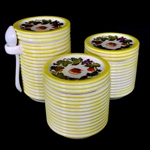 Puede incluir: Un juego de tres pilas de platos de cerámica blanca con rayas amarillas y blancas. Los platos tienen un diseño de frutas coloridas con un melocotón, uvas y fresas.