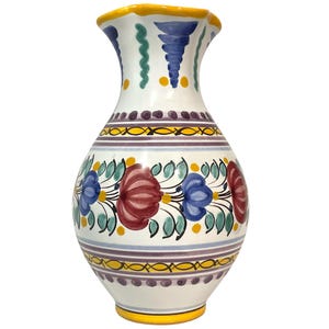 May include: A white ceramic vase with a flared, yellow-rimmed opening. The body features hand-painted floral motifs in red, blue, and green, accented by horizontal bands of purple and yellow. The design includes repeating leaf and petal patterns.