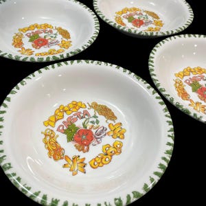 以下が含まれることがあります： 緑色の縁取りが施された、白いパスタボウルが4つ。各ボウルの中央には「PASTA」の文字と、トマト、パスタの形、その他の食材のイラストが描かれています。ボウルは黒い背景に置かれています。