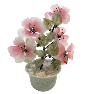 May include: A decorative floral arrangement with pink and white flowers, red accents, and green leaves. The flowers are in a pale blue ceramic pot filled with white pebbles. A unique home decor item.
