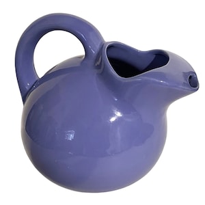 May include: A purple ceramic jug with a rounded body and a spout. The jug has a handle and a smooth, glossy finish.