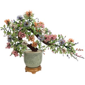 May include: A decorative bonsai tree with a brown trunk and branches, featuring colorful glass flowers in shades of pink, orange, white, and blue. The tree is planted in a light green ceramic pot with a wooden base.