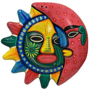 Puede incluir: Una placa decorativa de pared que presenta un rostro combinado de sol y luna. El lado del sol tiene una cara amarilla, mejillas verdes y rayos multicolores en azul, rojo y amarillo. El lado de la luna es rosa con un patrón floral y una media luna azul.