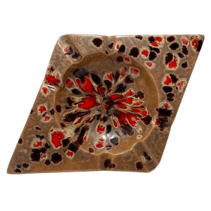 Puede incluir: Un cenicero de cerámica con forma de diamante con un esmalte moteado marrón y negro y patrones de remolino rojos y negros en el centro.