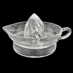 Peut inclure: Un presse-agrumes en verre transparent avec un motif côtelé et une poignée. Le presse-agrumes a un rémouleur conique au centre.