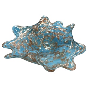 Puede incluir: Un cuenco de vidrio azul con una forma ondulada irregular y un diseño dorado moteado. El cuenco es perfecto para exhibir artículos decorativos o servir aperitivos.