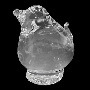 Puede incluir: Una escultura de vidrio transparente de un pájaro con un cuerpo redondeado y un pequeño pico. La escultura tiene un acabado liso y pulido y está diseñada para ser un objeto decorativo.
