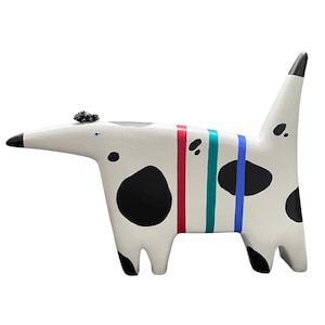 Pode incluir: Escultura de cão de cerâmica branca com manchas pretas e listras coloridas. O cão tem um focinho longo e uma cauda pontiaguda.