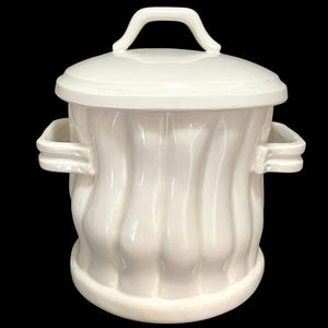 May include: A white ceramic container with a lid and handle. The container has a ribbed design and two side handles. The lid also has a handle. The container is likely for kitchen or home decor.