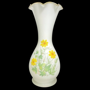 Op de afbeelding: Witte keramische vaas met een gegolfde bovenkant en een gouden rand. De vaas heeft een bloemenmotief met gele bloemen en groene bladeren.