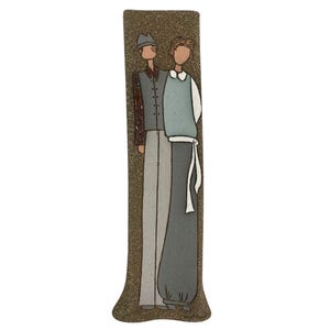 May include: A tall, rectangular ceramic vase with a textured, speckled brown background. The vase features a stylized illustration of two figures in neutral tones, one wearing a hat and vest, the other a sweater vest. The figures are standing close together.