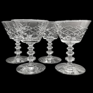 Puede incluir: Cuatro copas de champán de cristal transparente con patrones tallados en diamante en los cuencos. Los tallos tienen un diseño único de cuentas apiladas y las bases son redondas. Las copas están dispuestas sobre un fondo negro.