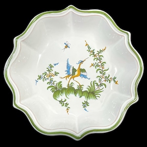 Op de afbeelding: Witte keramische serveerschaal met een geschulpte rand, met een handgeschilderd ontwerp van een vogel en bladeren in geel, blauw en groen. De rand heeft een groene rand met een roze accent. Een decoratief stuk om te serveren.