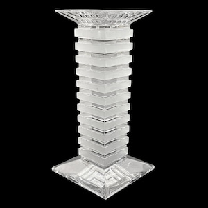 Può includere: Un portacandele in vetro trasparente con un design impilato. Il portacandele è alto e ha una base quadrata.