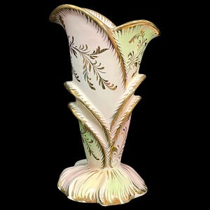 May include: A ceramic vase featuring a flared, petal-like rim and a wide, scalloped base. The surface is decorated with soft pastel pink and light green gradients, accented by intricate gold leaf filigree patterns along the edges and body.
