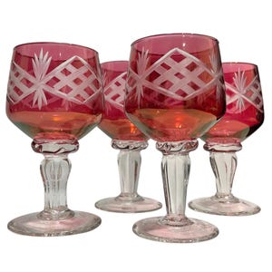Op de afbeelding: Een set van vier wijnglazen met dieprode kelken en stelen en voeten van helder glas. Het bovenste gedeelte van elke rode kelk is versierd met een wit geëtst ruitpatroon en stermotieven. De stelen hebben een opvallend geribbeld ontwerp.