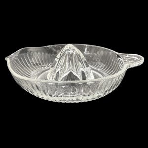 May include: A clear glass citrus juicer with a ribbed bowl and a central reamer. The juicer has a handle and a spout for easy pouring. The design is simple and functional, perfect for making fresh juice.