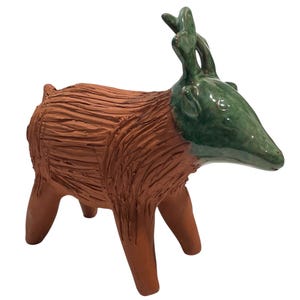 May include: A ceramic sculpture of a deer with a textured brown body and a green head. The deer has stylized antlers and is standing on four legs. The sculpture is likely handmade and has a rustic aesthetic.