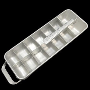 May include: A vintage aluminum ice cube tray with a handle and a lever marked "QUICKUBE". The tray is divided into rectangular compartments for ice cubes. The tray is silver and sits against a black background.