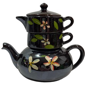 May include: A stackable tea set consisting of a large teapot at the base, a teacup in the middle, and a small teapot with a lid on top. The set is made of glossy black ceramic and features hand-painted white and pink flowers with green leaves.