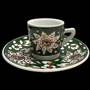 May include: A green and white ceramic coffee cup and saucer set with a floral design. The cup and saucer are decorated with white flowers with orange centres on a green background.