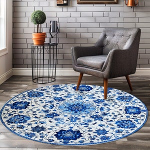 May include: A round blue and white floral area rug with a traditional design. The rug is placed on a wood floor in a living room setting with a gray armchair and a black metal side table.