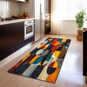 Puede incluir: Una alfombra geométrica colorida con fondo negro y un patrón de círculos y cuadrados superpuestos en tonos de rojo, amarillo, naranja, azul y gris. La alfombra está colocada sobre un suelo de madera en una cocina.