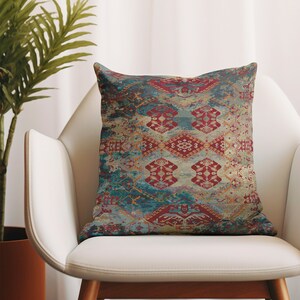 Puede incluir: Una almohada decorativa con un patrón geométrico colorido en tonos azules, rojos y dorados. La almohada está sentada en una silla blanca.