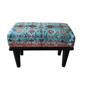 A colorful, patterned ottoman or footstool with a blue and orange design, placed on a black wooden base.