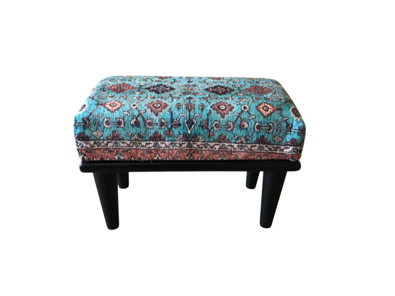A colorful, patterned ottoman or footstool with a blue and orange design, placed on a black wooden base.