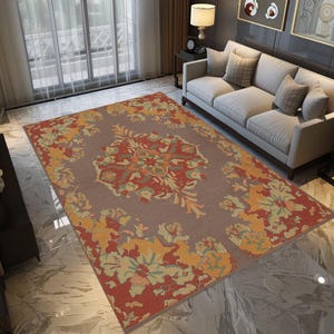 May include: A rectangular area rug with a central floral medallion design in shades of red, orange, and green on a taupe background. The rug features a floral border in yellow, orange, and green. The rug is placed on a marble floor.